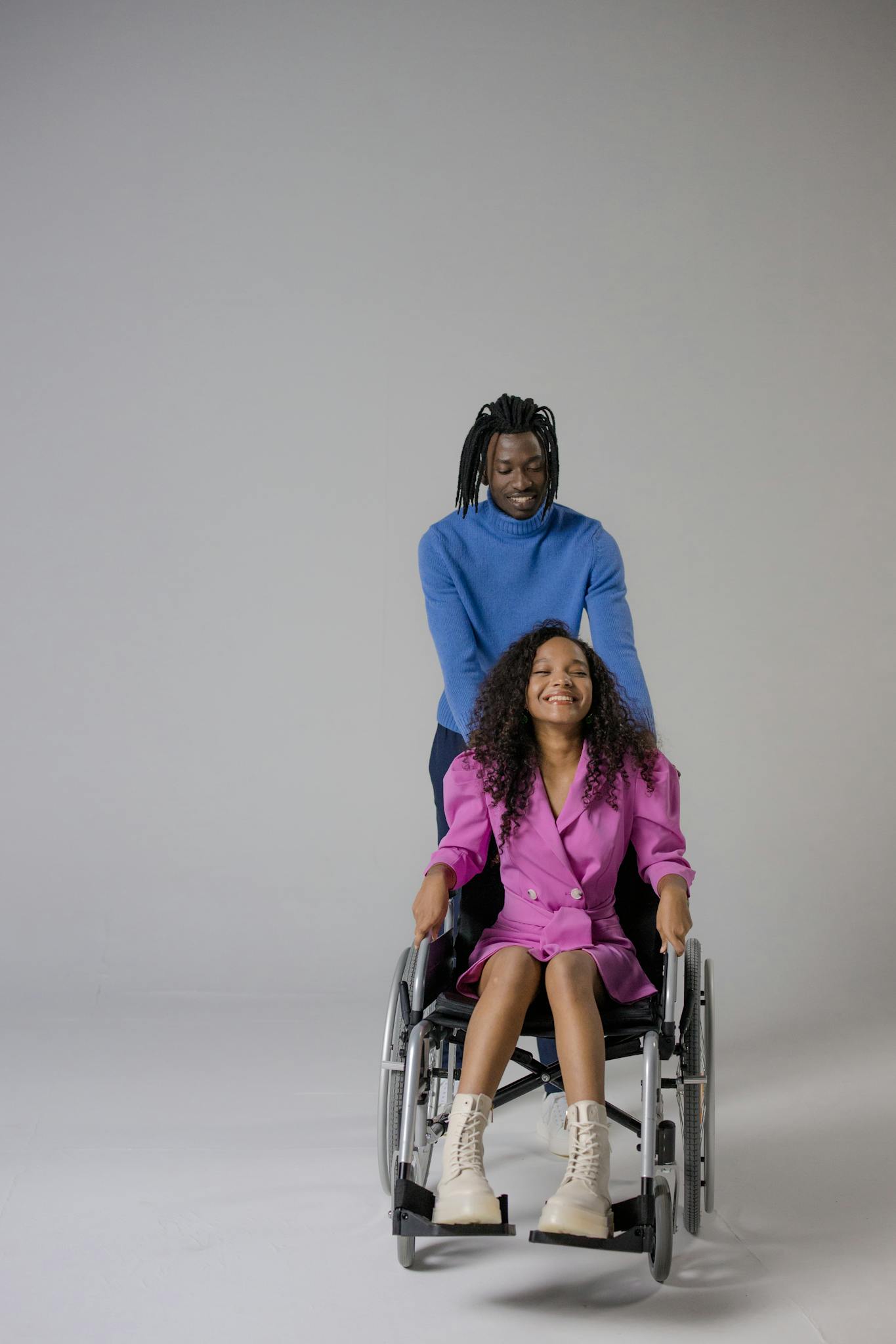 A black man smiling while assisting a woman in a wheelchair indoors.