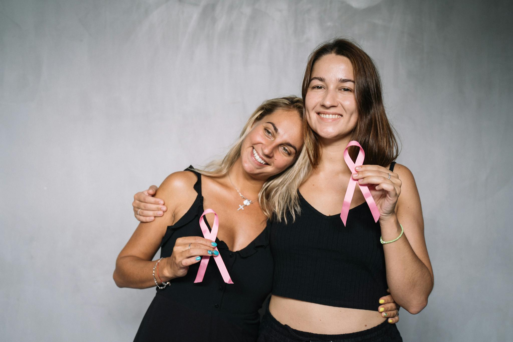 Two women smiling and holding pink ribbons to support breast cancer awareness.